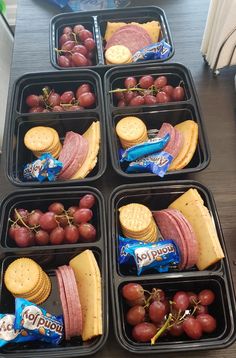 four trays filled with grapes, crackers and other snacks on top of a table