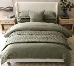 a bed with green comforter and pillows in a room next to two nightstands