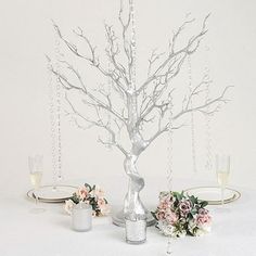 there is a silver tree with flowers on it and candles in the vases next to it