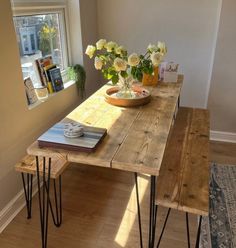 a wooden table with hairpin legs and flowers in a bowl on top, next to a window