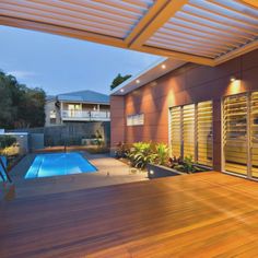 a wooden deck next to a swimming pool with lights on the ceiling and windows above it