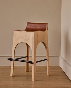 a wooden stool with a leather seat on the floor next to a white wall and wood floors