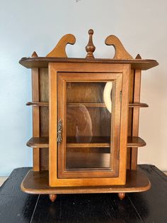 an old wooden cabinet with glass doors on the top and bottom shelf is sitting on a black table