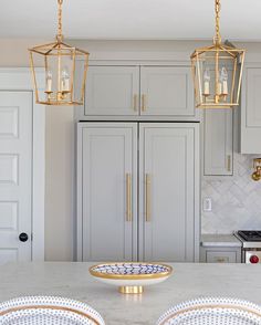 a kitchen with white cabinets and gold accents on the counter top, along with two pendant lights hanging from the ceiling