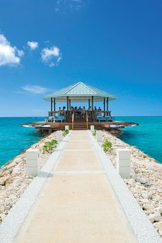 people are sitting at the end of a pier on an island in the middle of the ocean