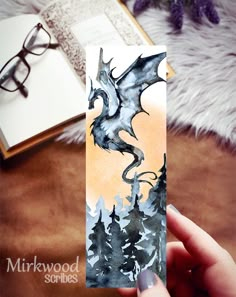 a hand holding up a card with a dragon on it and trees in the background