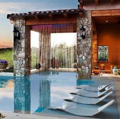 an outdoor swimming pool surrounded by stone pillars and windows with drapes on the side