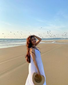 a woman standing on top of a sandy beach next to the ocean wearing a white dress