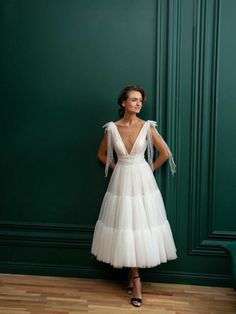 a woman standing in front of a green wall wearing a white dress with ruffles