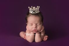 a baby with a crown on its head is laying down and looking at the camera