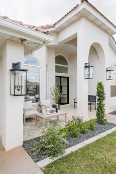 a white house with lots of windows and plants in the front yard, along with an outdoor seating area