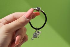 a hand holding a small dog charm on a black cord with a silver bead around it