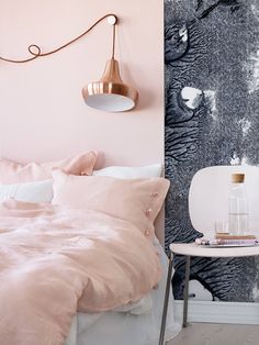 a bed with pink sheets and pillows in a white room next to a wall light