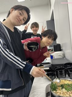 three young men preparing food in a kitchen with pots and pans on the stove