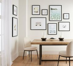 a dining room table with two chairs and pictures on the wall above it in black frames