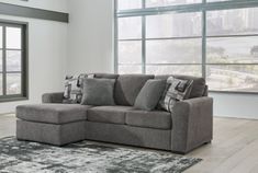 a living room with large windows and a gray couch in front of a rug on the floor