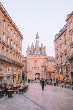 people are sitting at tables in the middle of an old town square with tall buildings