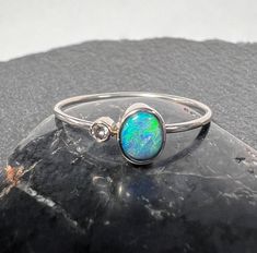 Australian black opal with natural diamond accent stacker ring set in 14k white gold. 14k white gold opal stacker ring. Cute little itty bitty 5.3mm x 4.25mm .38 carat Australian black opal from Lightning Ridge. 1.9mm natural G/H SI diamond .027 carat. 14k white gold (not rhodium plated) band and bezels. 1mm round solid 14k white gold band. Currently US size 8 for scale (select size at checkout). Hand made, one of kind All of our creations are made out of 14K Gold (Yellow, White, Rose) or 925 Sterling Silver, None are filled or electroplated.  All of our stones are Nature-made, therefore some natural flaws may be present. Hand crafted in the We Work Gems Shop in Washington State. Size and weight are approximate. Please feel free to ask any questions. Back to our shop https://www.etsy.com/s Black Opal Jewelry Rings, Opal And Black Diamond Ring, Black Opal Diamond Ring, Black Australian Opal Ring, Black Opal Ring Opal Auctions, Elegant Adjustable Opal Stackable Rings, Oval Opal Jewelry With Bezel Setting, Oval Opal Rings With Bezel Setting, Elegant Silver Opal Stackable Rings