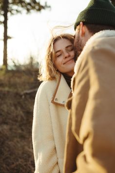 a man and woman standing next to each other in front of some trees with the sun shining on them