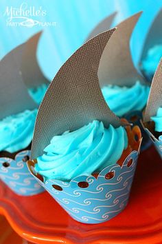 cupcakes with blue frosting and a shark fin on top are sitting on an orange plate