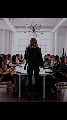 a woman standing at a table in front of a group of people sitting around it