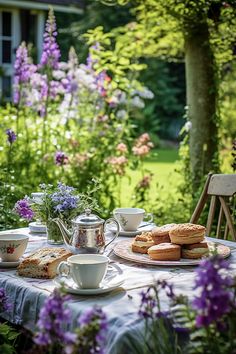 the table is set with tea and pastries in front of purple flowers on the lawn