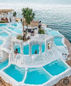 people playing in an artificial swimming pool on the beach with palm trees and blue water