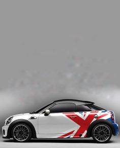 a small white car with a british flag painted on it's side, parked in front of a gray background