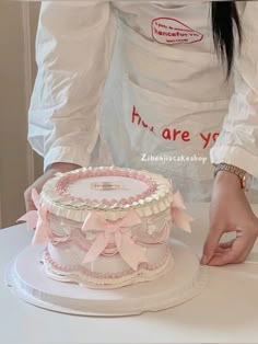 a woman is decorating a cake with pink ribbon and bows on the bottom tier