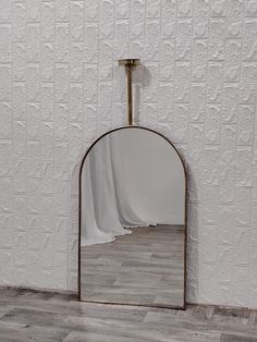 a mirror sitting on top of a wooden floor in front of a wall covered in white sheets