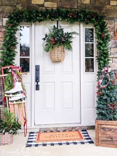 a front door decorated for christmas with wreaths and potted plants next to it