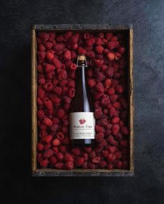 a bottle of beer surrounded by raspberries in a wooden box on a black surface