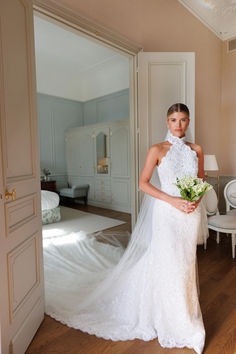 a woman in a white wedding dress standing next to a bed and doorway with her hand on her hip