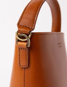 This classy bucket bag has a roomy interior and a slip-in pocket to grab your small essentials in a sec. Designed with a flat bottom, Bobbi stands on her own, making a true statement. Carry her with the top handle or wear her as a cross body bag. Want to spice things up? Her dog hook clasp allows you to mix and match our Webbing straps! Bobbi enjoys a night out or a trip to the beach. She's our go-to girl for every occasion. Check out Bobbi Bucket Bag Maxi, her newer bigger sister! OMB-E139BV Classic Bucket Bag With Leather Handles For Business, Classic Business Bucket Bag With Leather Handles, Classic Bucket Hobo Bag With Detachable Handle, Classic Bucket Bag With Detachable Handle For Business, Classic Business Bucket Bag With Detachable Handle, Classic Office Bucket Bag With Leather Lining, Classic Leather-lined Office Bucket Bag, Classic Everyday Bucket Bag With Smooth Grain, Cognac Bucket Bag With Leather Handles