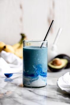 a glass filled with blue liquid sitting on top of a counter next to an avocado