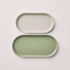 two oval trays sitting next to each other on a white surface with green trim