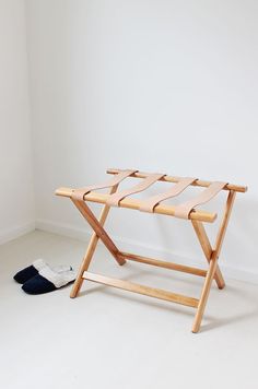 a small wooden folding chair next to a pair of slippers on the floor in front of a white wall