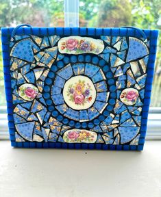 a blue and white mosaic tile with roses on it, sitting in front of a window