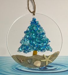 a glass ornament with a blue christmas tree in the center and starfish on the bottom