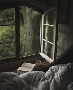 an open window with a book and cup sitting on the bed in front of it