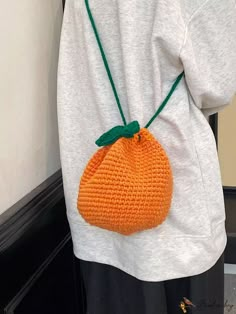 an orange crocheted bag hanging from a woman's white shirt in front of a door