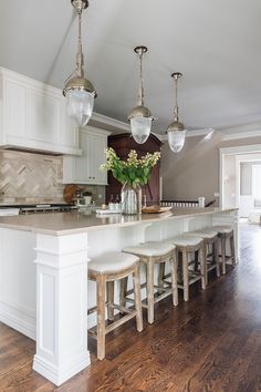 a kitchen island with stools and lights hanging from it's ceiling over the counter