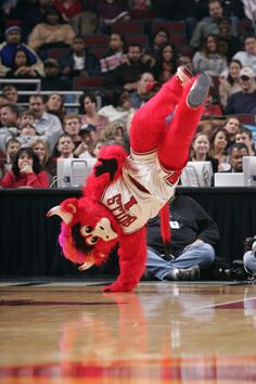 a mascot doing a handstand in front of an audience at a basketball game