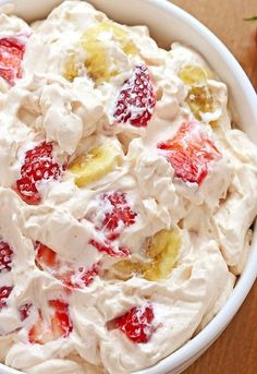 a white bowl filled with fruit salad on top of a wooden table next to strawberries