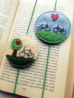 two felt brooches with bicycles on them sitting on top of an open book