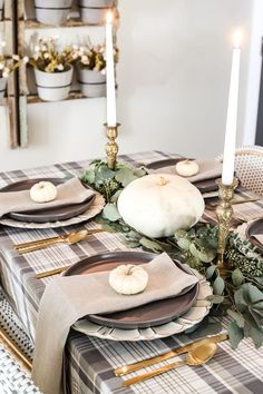 the table is set for thanksgiving dinner with pumpkins, greenery and candlesticks