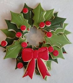 a christmas wreath made out of cookies with holly leaves and red berries on it, sitting on a white surface