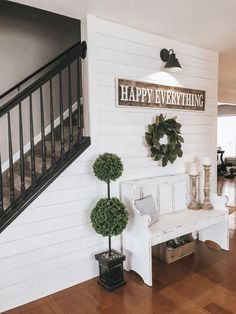 there is a white bench in the middle of this living room with two potted plants and a happy everything sign on the wall