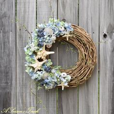 a wreath with blue flowers and seashells is hung on a wooden fence next to a starfish