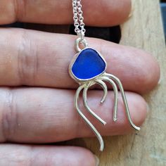 a hand holding a necklace with a blue stone in the shape of a jellyfish